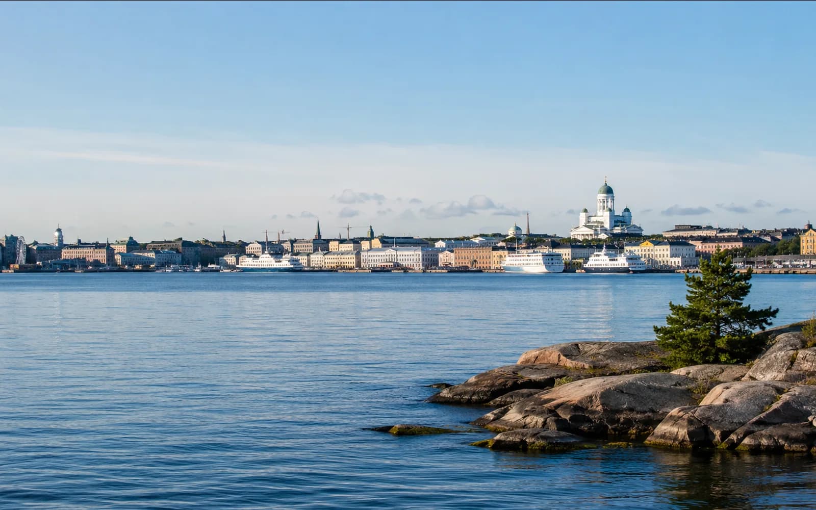 Helsinki-style Finnish waterfront skyline across calm blue water and rocky shoreline