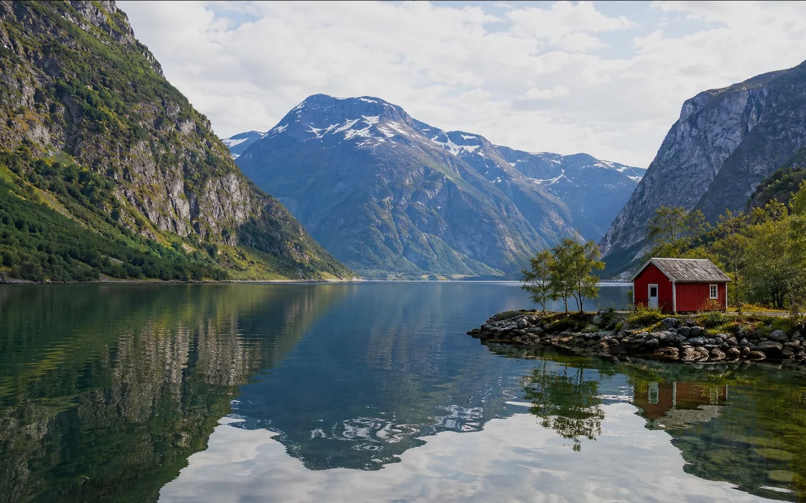 Norwegian fjord landscape with mountains, reflective water and a red cabin on the shoreline